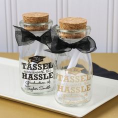 three glass bottles with cork tops on a white serving tray, one has a black bow and the other is empty