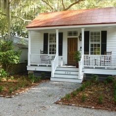 a small white house with black shutters and a red roof on the front porch