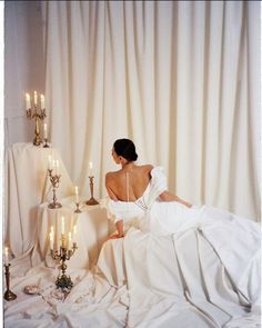 a woman in a white dress sitting on top of a bed next to some candles