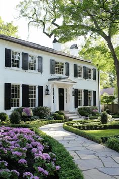 a large white house with black shutters on the front and side windows, surrounded by lush greenery