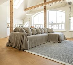 a living room filled with lots of furniture under a large window covered in blankets and pillows