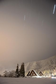 the night sky is lit up with stars above houses and snow covered trees in the foreground