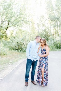 an engaged couple standing on the road in front of trees during their engagement photo session