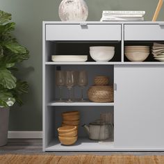 an open cabinet with dishes and glasses on the shelves next to a potted plant