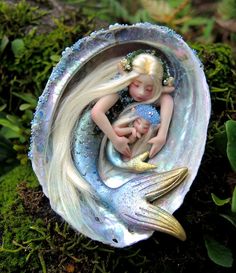 there is a little mermaid and her baby in a shell on the mossy ground