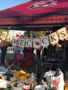 people are standing under a red tent with signs that read gamecocks and other items