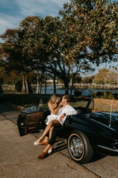 a man and woman sitting on top of a black car