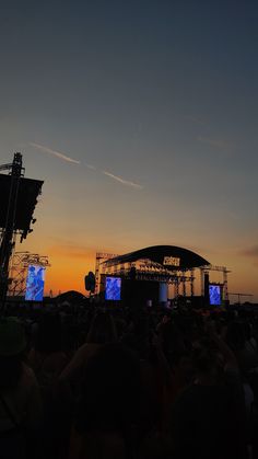 the stage is set up for an outdoor concert at sunset or sunrise, with two large screens on each side of the stage