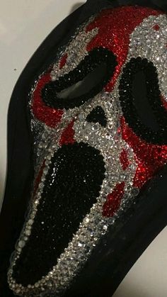 a red and black mask with silver sequins on the face is sitting on a white surface