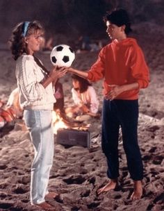 two people standing on the beach with a soccer ball in their hand and one person holding it