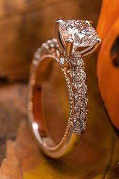 a close up view of a diamond ring on a wooden surface with an orange pumpkin in the background