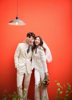 two people are posing for a photo in front of a red wall wearing white suits