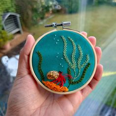 someone is holding up a hand embroidered hoop with an image of a crab and seaweed on it