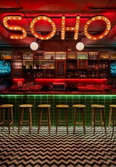 a bar with stools and neon signs above it