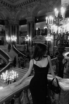 a woman in a black dress is standing at the top of an escalator