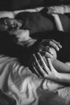 black and white photograph of two people laying in bed with their hands on each other