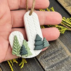 a hand holding a small ceramic ornament with trees on it's side