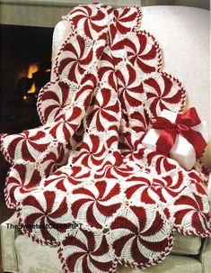 a red and white afghan sitting on top of a couch next to a fire place