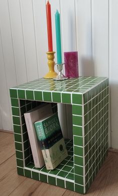 a small green table with books and candles on it, next to a white wall