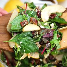 a salad with spinach, apples and cranberries in a glass bowl on a wooden spoon