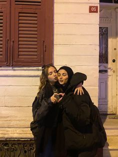 two women standing next to each other in front of a building