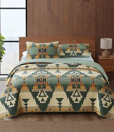 a bed covered in a green and orange quilt next to a wooden headboard with a window