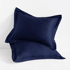 two blue pillows sitting next to each other on top of a white bed covered in dark blue sheets