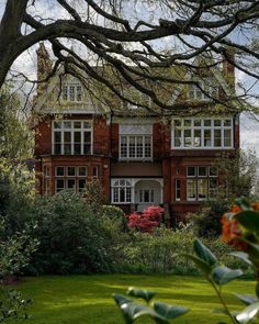 a large red brick house surrounded by lush green grass and trees in the foreground