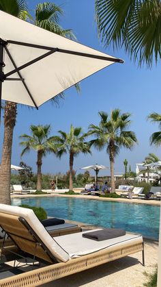 an empty pool with lounge chairs and umbrellas next to the swimming pool, surrounded by palm trees