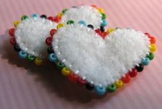 two white heart shaped brooches sitting on top of a pink cloth covered table