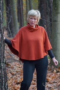 a woman standing next to a tree wearing an orange ponchy top and black pants