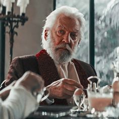 an old man sitting at a table with wine glasses