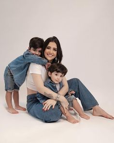 a woman sitting on the floor with two children and holding her arms around her shoulders