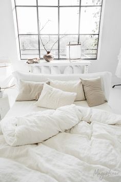 an unmade bed with white sheets and pillows in front of a large windowsill