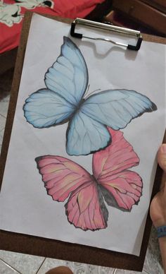 a drawing of two blue and pink butterflies on a piece of paper in front of someone's hand