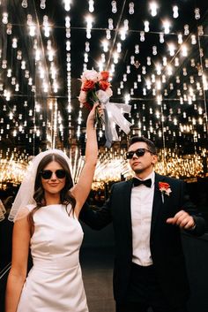 a bride and groom holding up their bouquets in front of the ceiling with lights