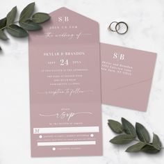 the wedding stationery is laid out on a marble table with greenery and rings