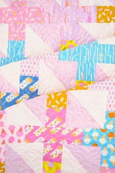 a colorful quilt is laying on top of a bed sheet that has pink, blue, yellow and white designs