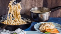 someone is lifting noodles out of a skillet on a table with other dishes and utensils