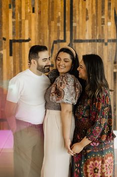 three people standing next to each other in front of a wooden wall