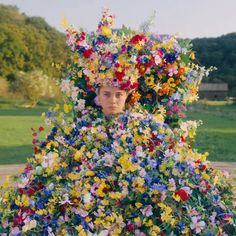 a woman with flowers on her head is standing in front of a large pile of flowers