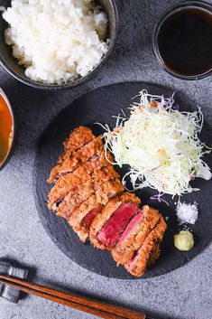 a plate with meat, rice and chopsticks on it next to bowls of sauce