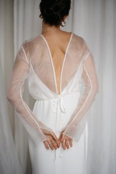 the back of a woman wearing a white dress with sheer sleeves and an open neckline