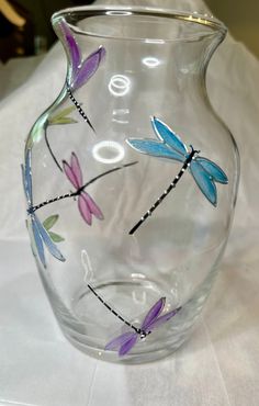 a glass vase with dragonflys painted on the outside and inside, sitting on a white table cloth