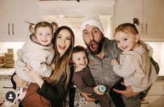 a group of people standing in a kitchen with one holding a baby and the other holding an infant