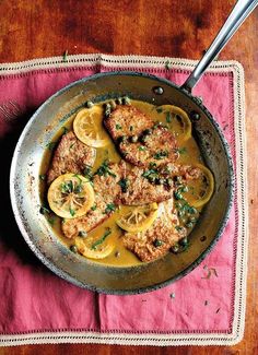 a skillet filled with meat and lemons on top of a pink place mat