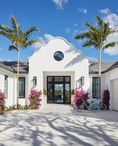 a bike is parked in front of a white house with palm trees and pink flowers