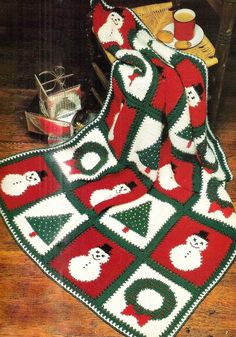 a crocheted christmas afghan with santas and snowmen on it, sitting on a wooden floor