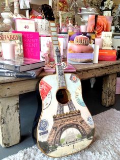 a guitar sitting on top of a wooden table next to a pile of books and candles