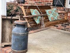 a wooden swing sitting on top of a porch next to a blue trash can and brick wall